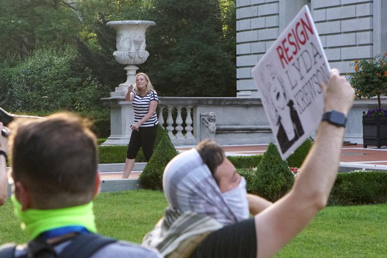This image shows the woman moving towards the protesters who are peaceful. She points a gun towards them. She still has her finger on the trigger.