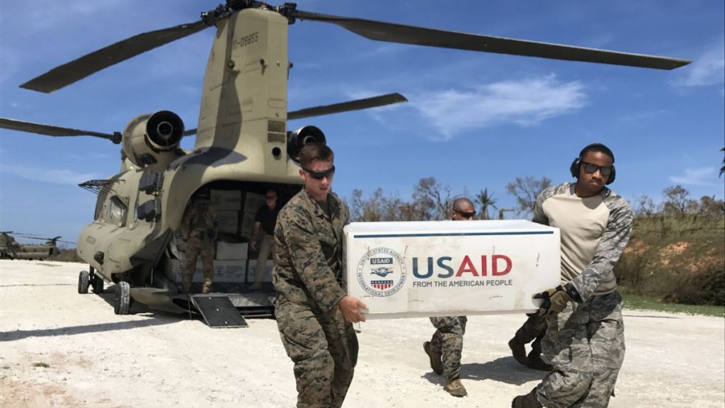 American troops unload boxes of "US Aid" from the rear of a Chinook helicopter.